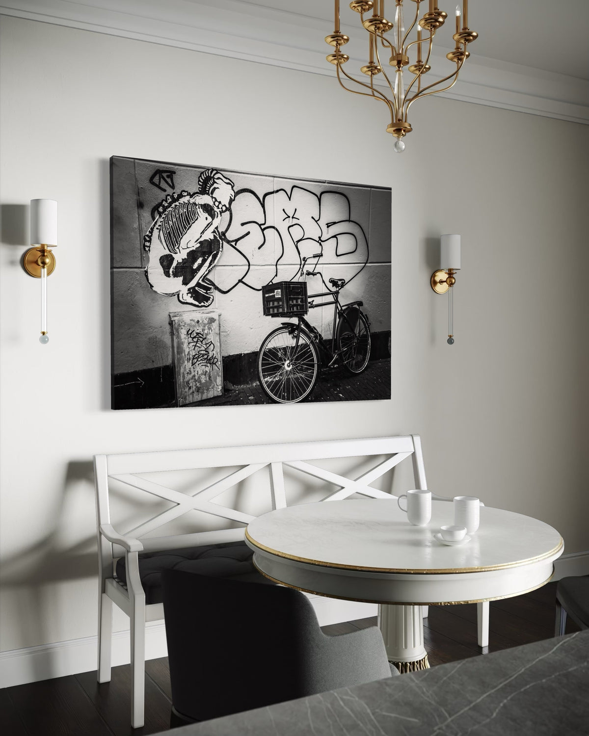 Street & Steel print on a white wall above a white bench and a round white table, between two brass wall sconces under a brass chandelier