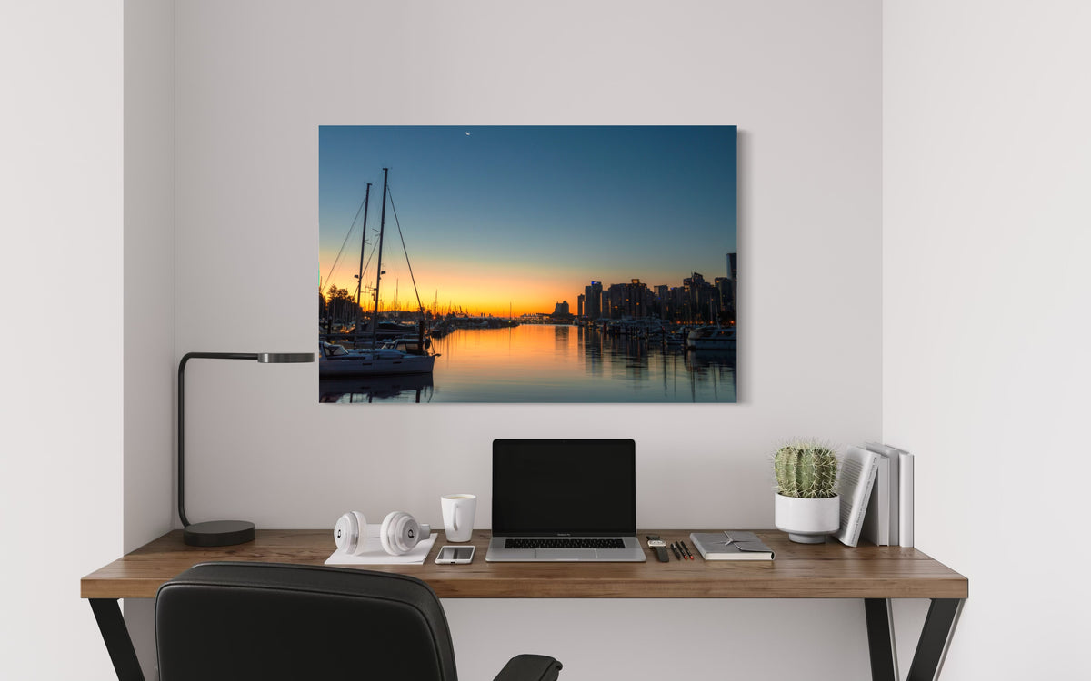 Vancouver Sunrise print above a wooden desk with a laptop, white headphones, a black desk lamp and a potted cactus
