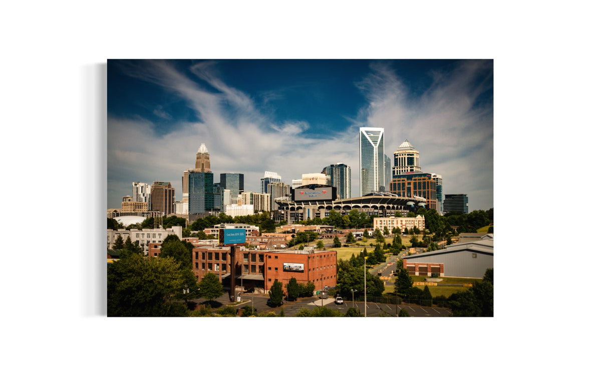 Queen City print of uptown Charlotte towers and Bank of America Stadium under wispy clouds, shown as a mounted print