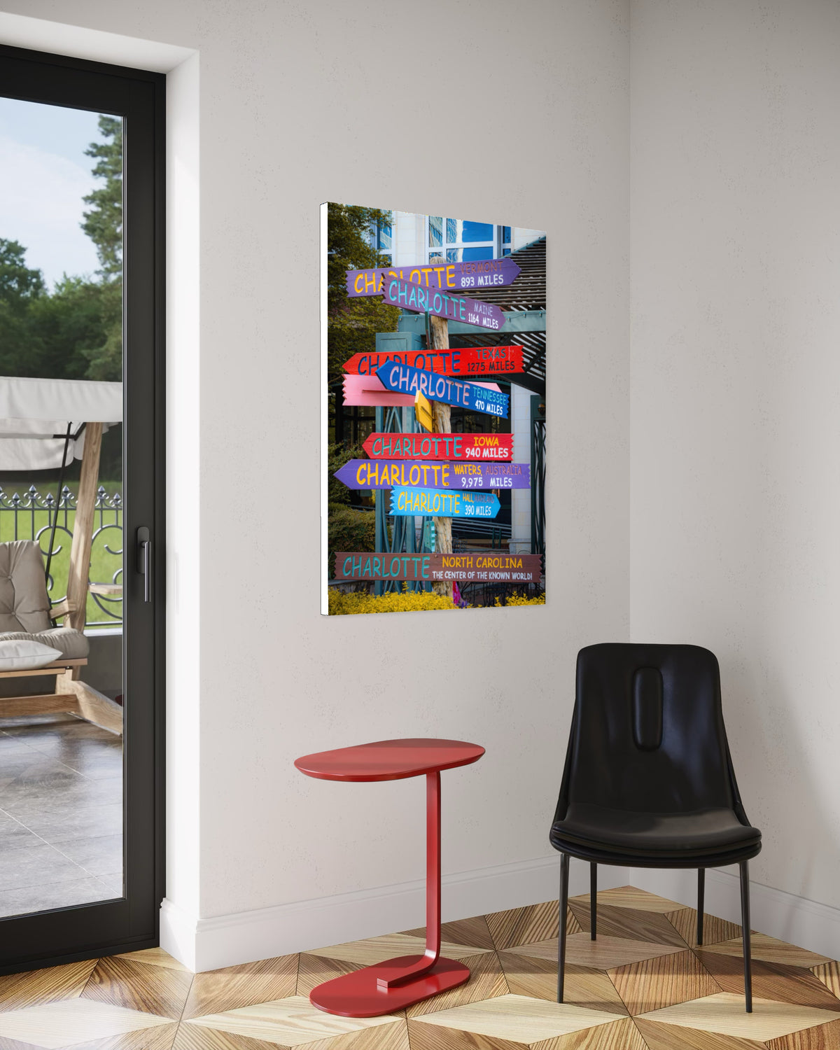 Directions print of the colorful Charlotte signpost on a white wall above a red side table and a black leather chair, beside a glass door to a patio