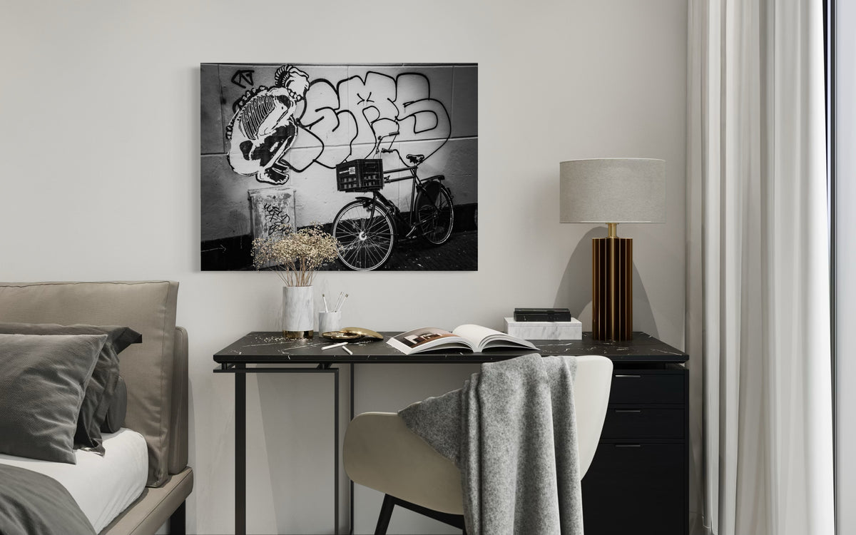 Street & Steel print above a black marble desk with a gold table lamp and dried flowers, beside a bed