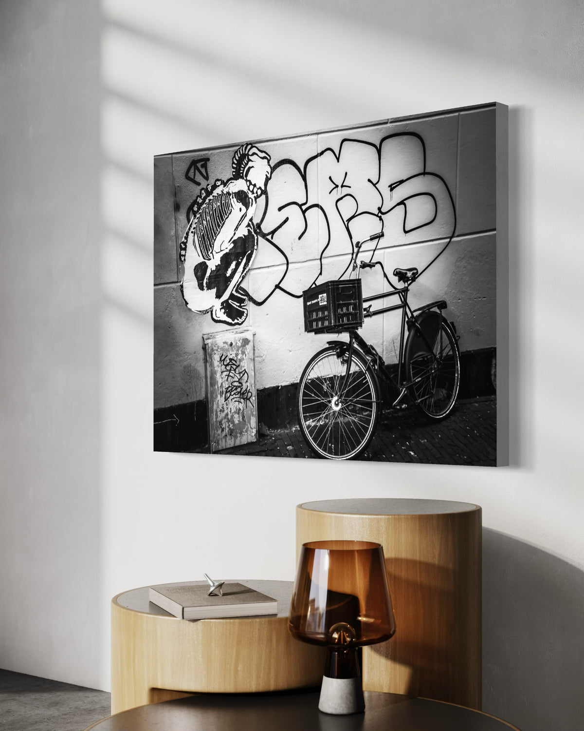Street & Steel print on a sunlit wall above round wooden side tables and an amber glass lamp
