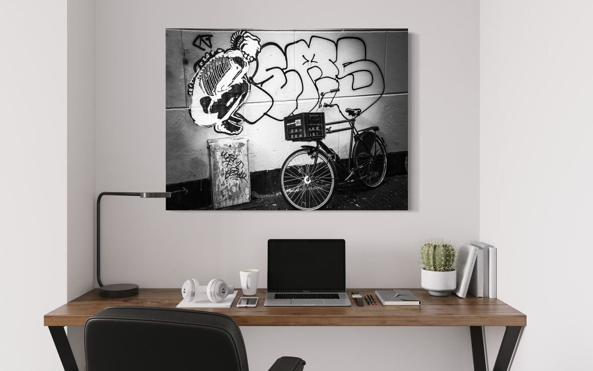 Street & Steel print above a wooden desk with a laptop, white headphones, a black desk lamp and a potted cactus
