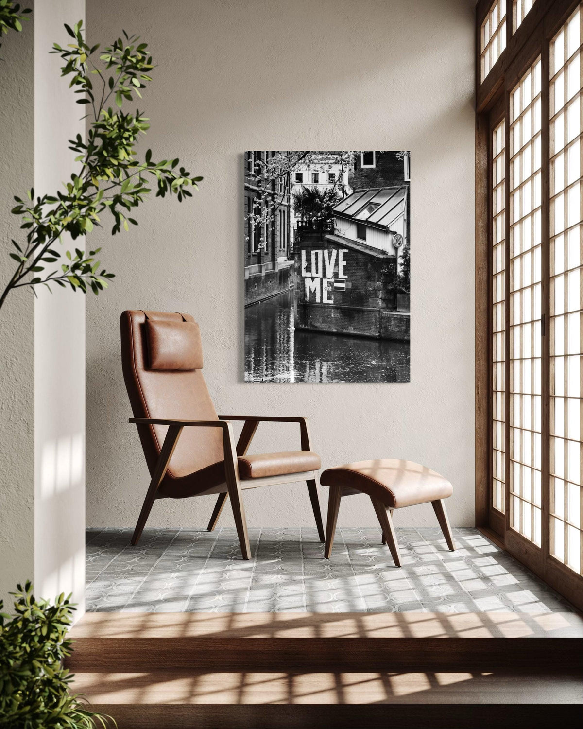 Love Me print on a wall beside a brown leather lounge chair and footstool near tall paned windows