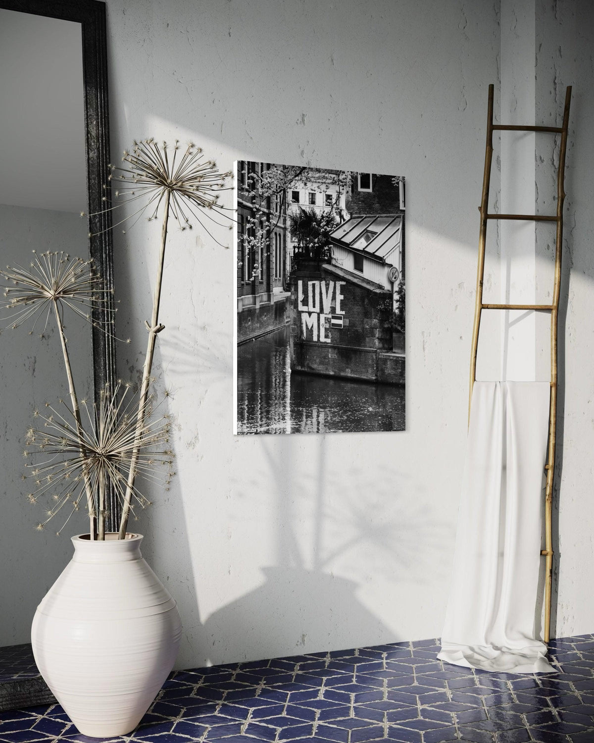 Love Me print on a white wall beside a tall vase of dried flowers and a wooden ladder